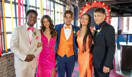 A group of teens with vibrant tuxedos and dresses in prom