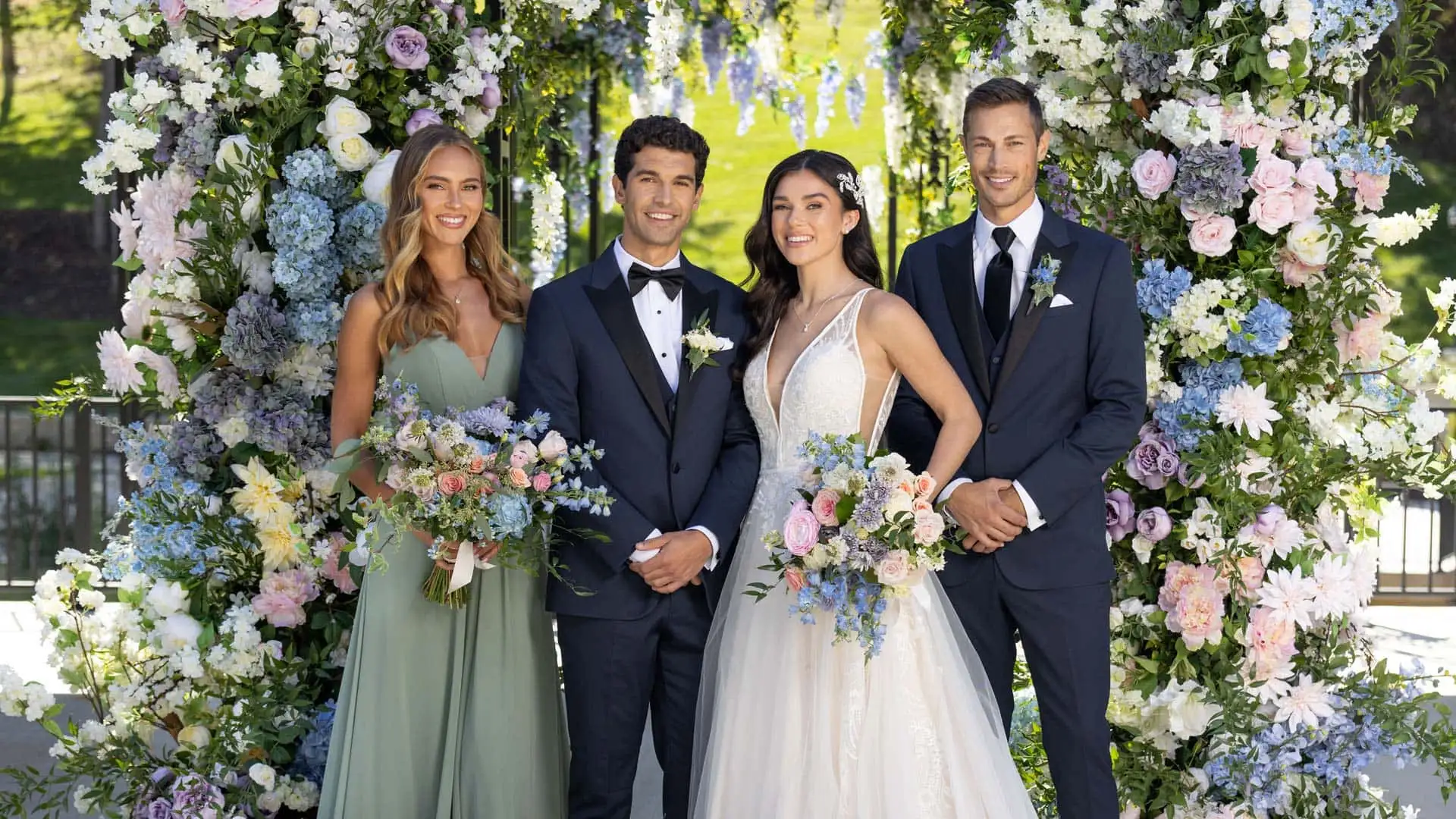 A groom and bride with friends taking a picture infront of the floral arch